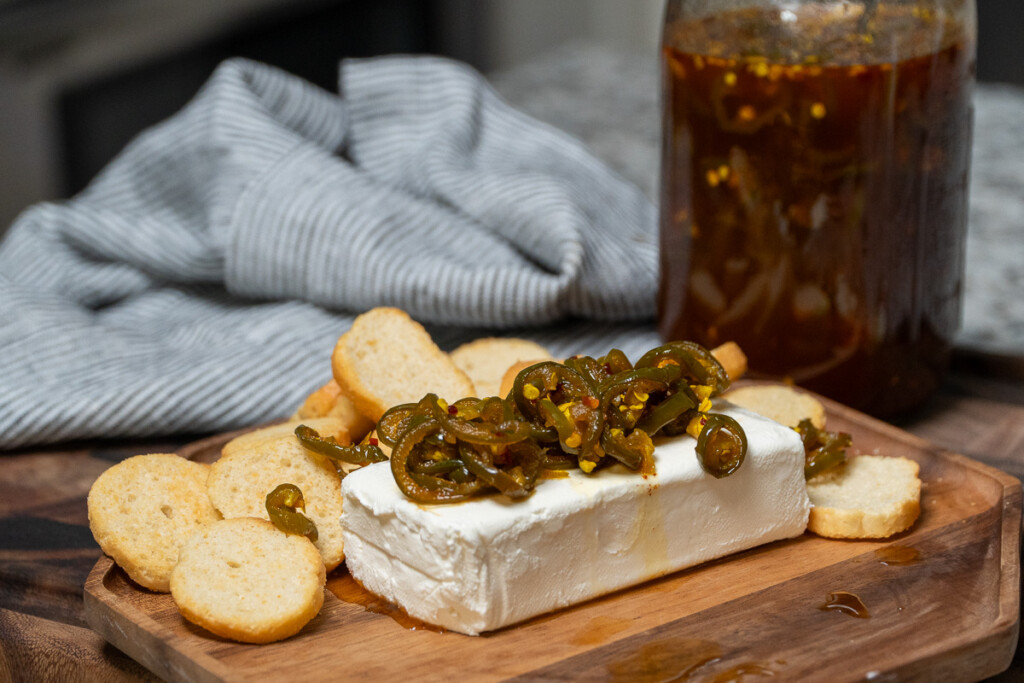 a block of cream cheese with cowboy candy on top, crackers on the side and jar in the background