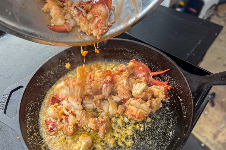 lobster being poured from a bowl into a cast iron pan