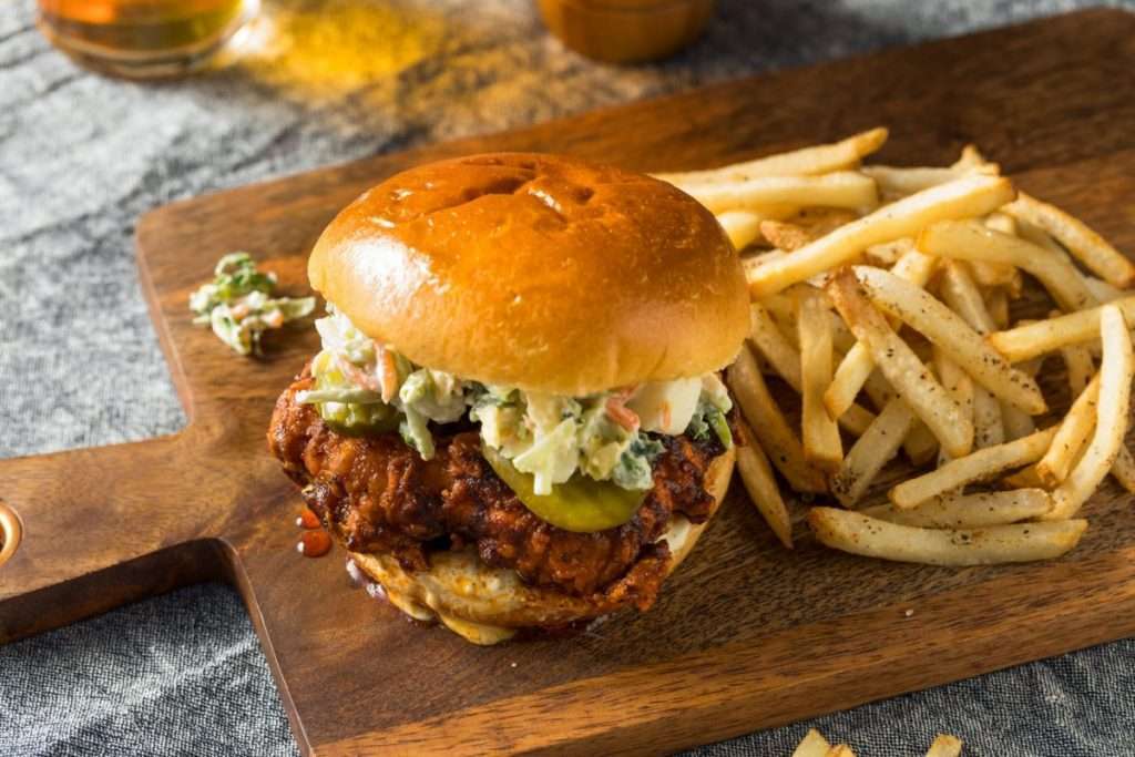 Nashville Hot Chicken sandwiches with fries on a cutting board.