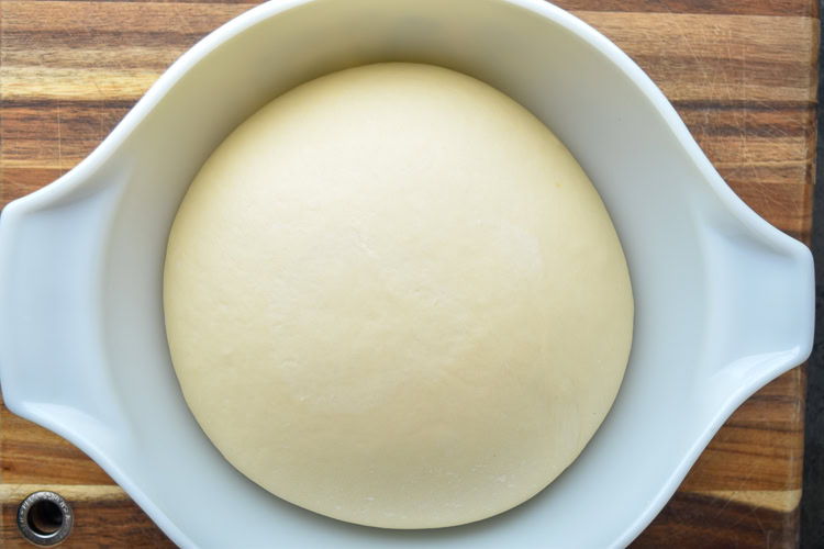 a ball of brioche dough in a white bowl after 45 minutes