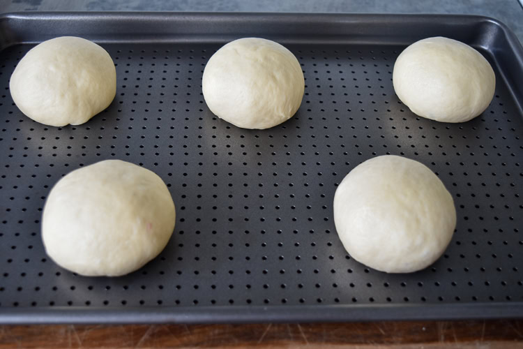 formed brioche buns on a metal baking tray with holes