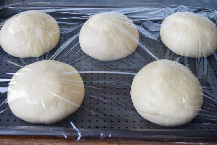 brioche buns risen on a baking tray with plastic wrap over the top