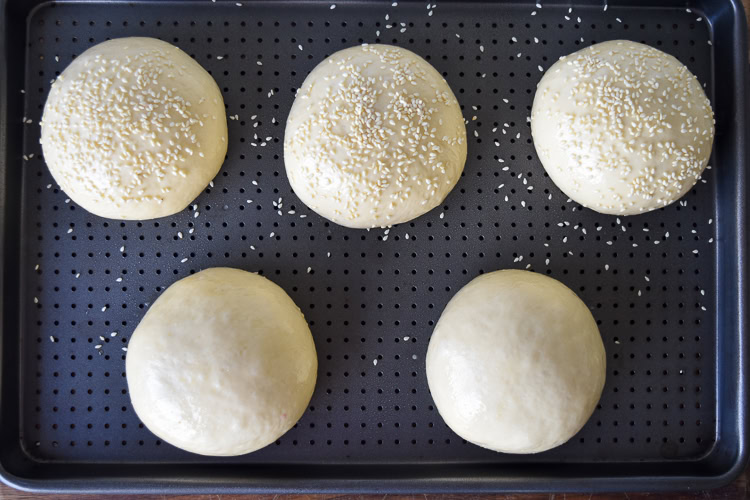 five uncooked brioche buns with eggwash on a metal tray