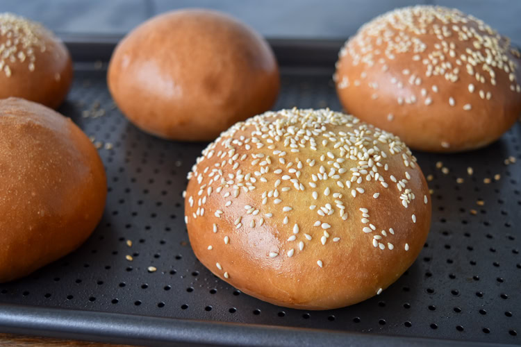 cooked brioche burger buns on a metal tray