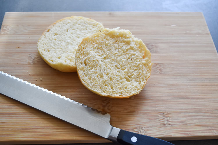 brioche burger bun cut in half on a wooden board with a knife