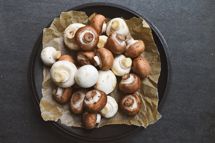 a black bowl with brown paper full of button and cremini mushrooms