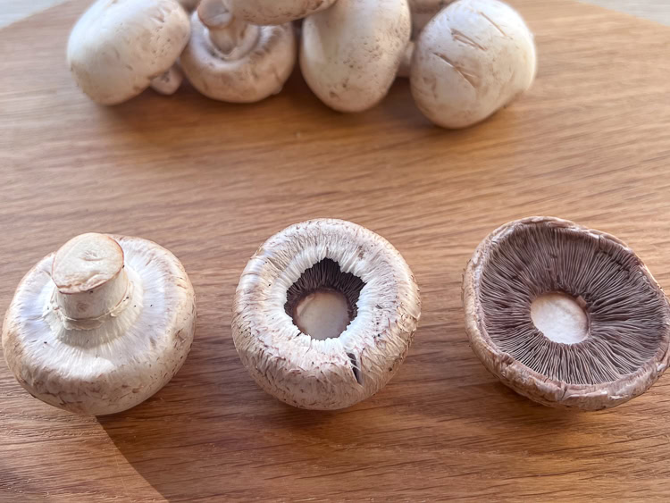 a mushroom with a stem, a mushroom without a stem, a trimmed mushroom on a wooden board