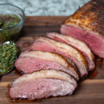 smoked and sliced picanha on a wood chopping board with a spoon full of chimichurri sauce