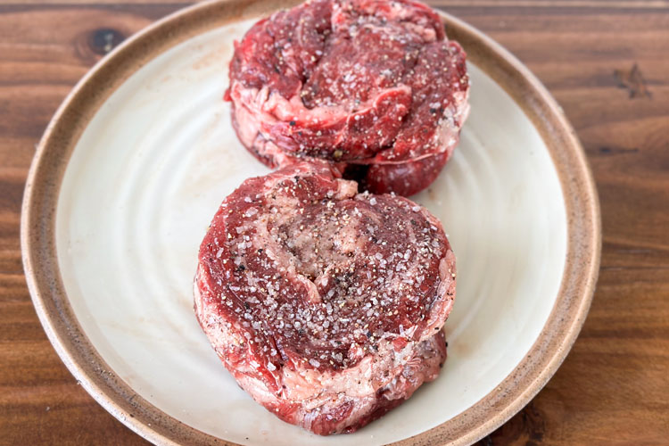 two seasoned raw ribeye caps on a white plate