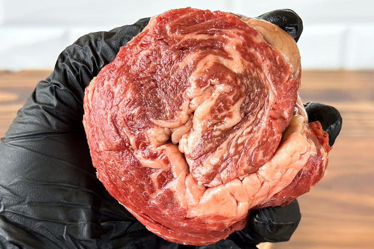 a black gloved hand holding a ribeye cap steak