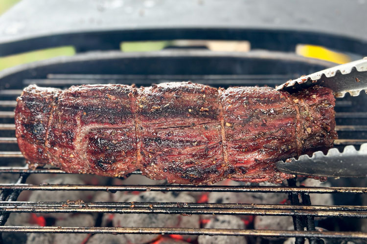 whole beef tenderloin on grill being turned with tongs