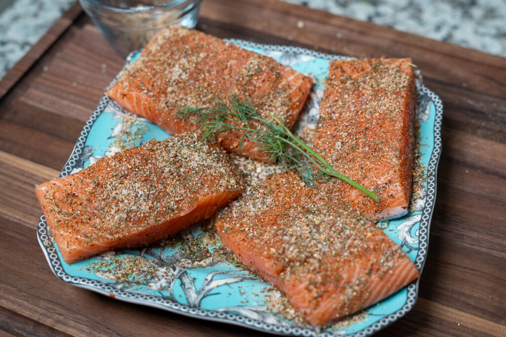 four filets of raw seasoned salmon on a blue plate