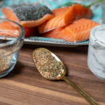 spoonful of salmon rub on table with jar of rub and filets of raw salmon in the background