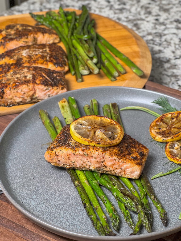 salmon with lemon on top sitting on cooked asparagus on a grey plate