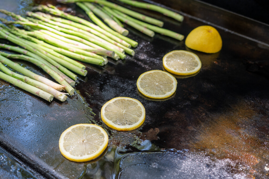 salmon slices on the griddle with asparagus in the background