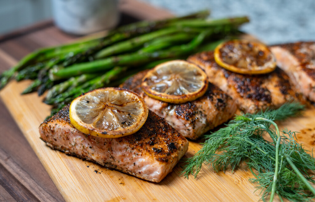 salmon filets with lemon slices on the top on a wooden board