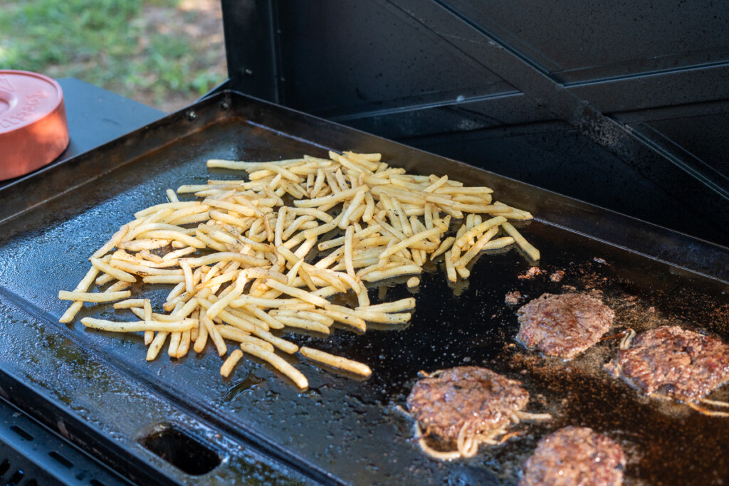 French fries on the griddle with burgers beside them