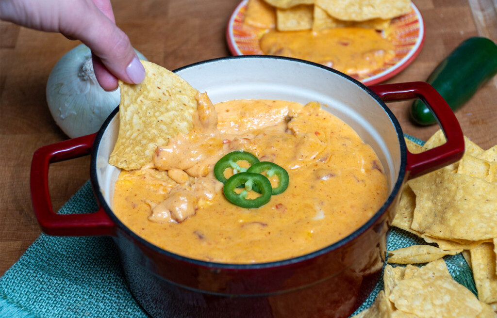 smoked queso dip in a serving dish with a tortilla being dunked in it.