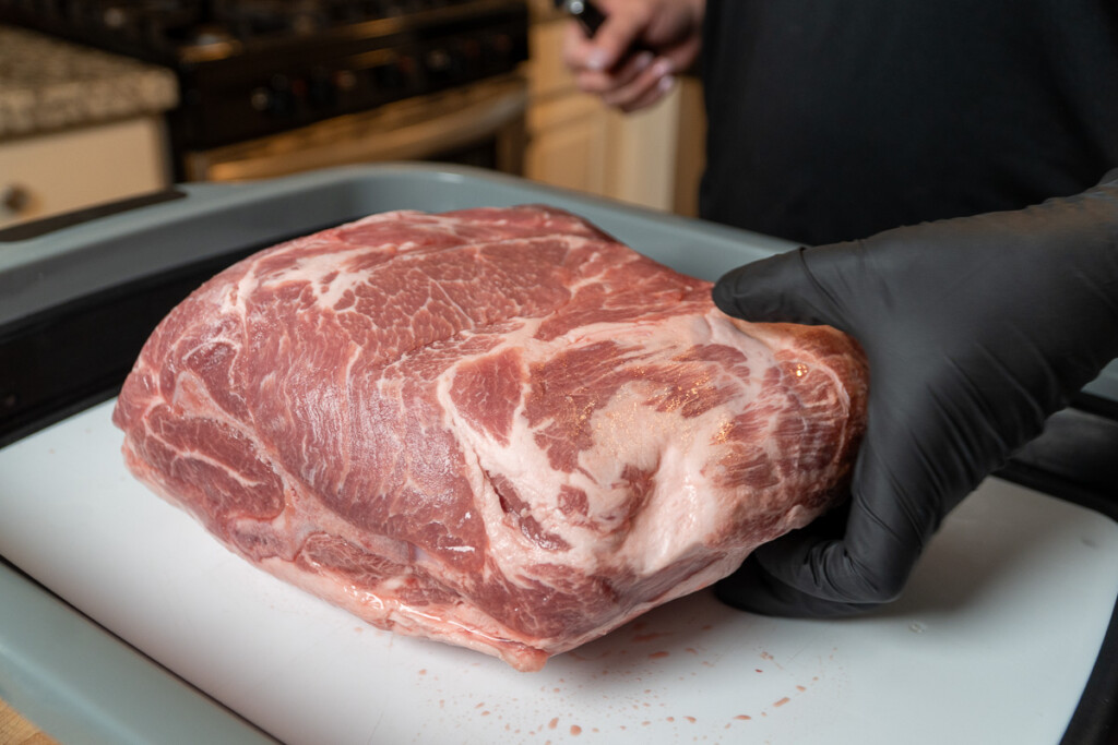 a raw piece of pork butt on a white chopping board