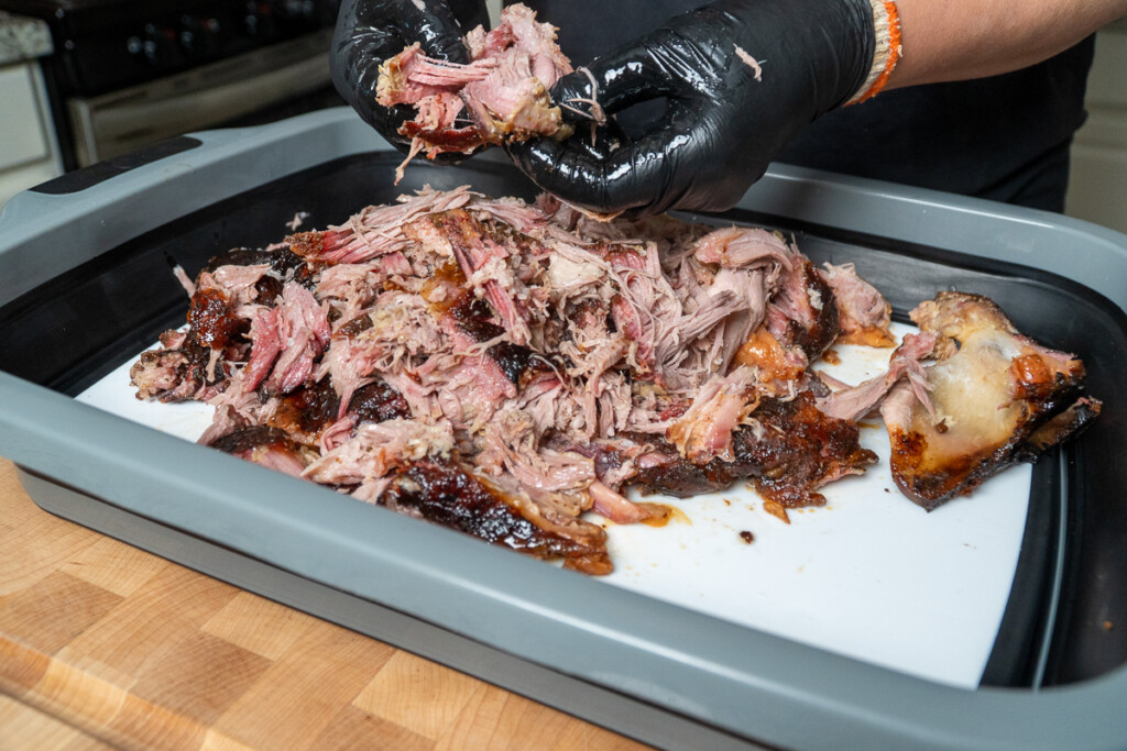 black gloved hands shredding a smoked pork butt