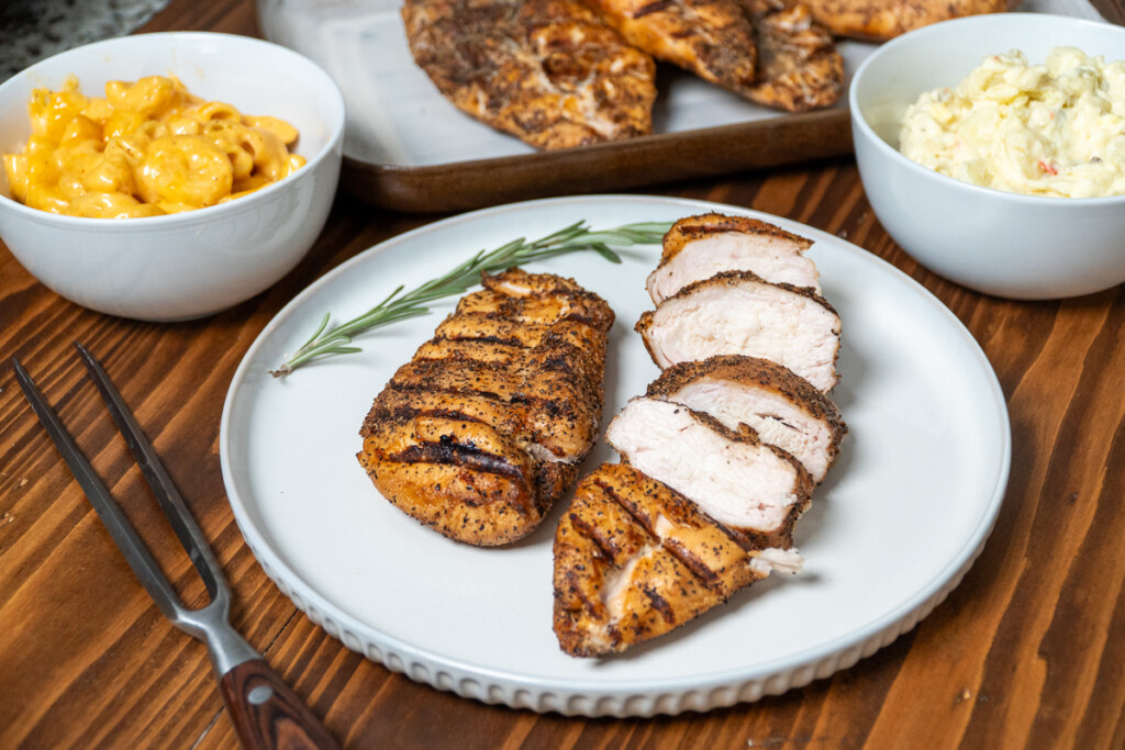 one whole and once sliced up cooked chicken breast on a white plate