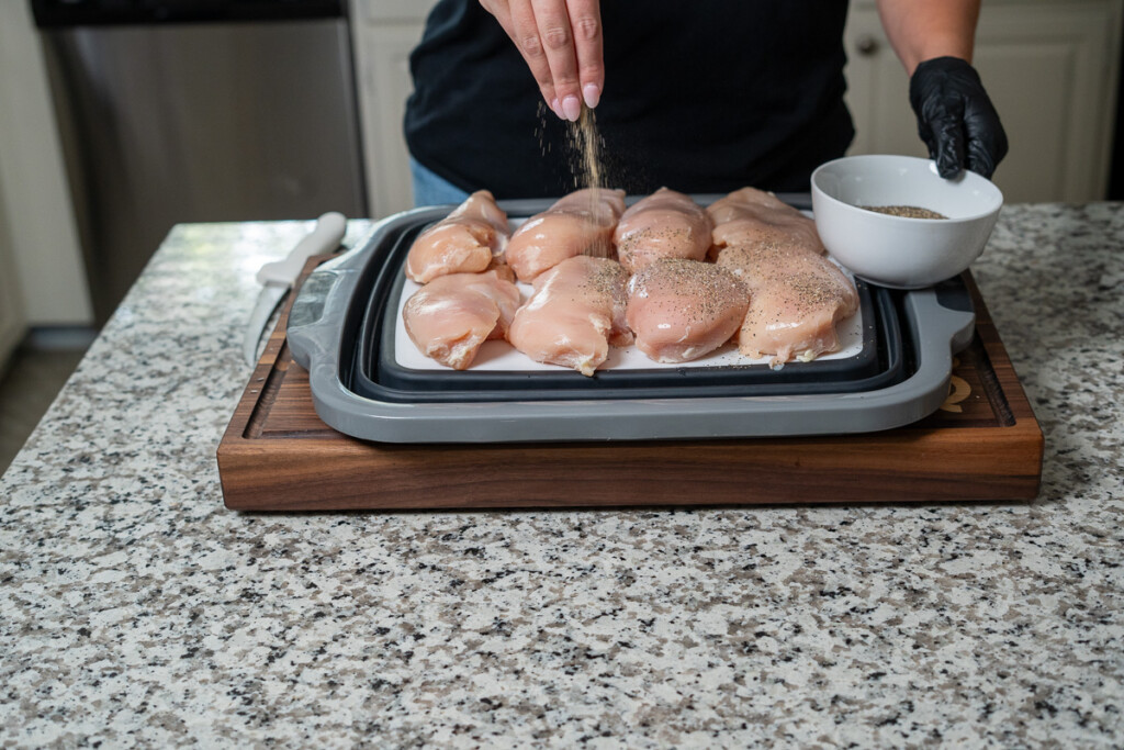 a hand sprinkling seasoning onto raw chicken breasts