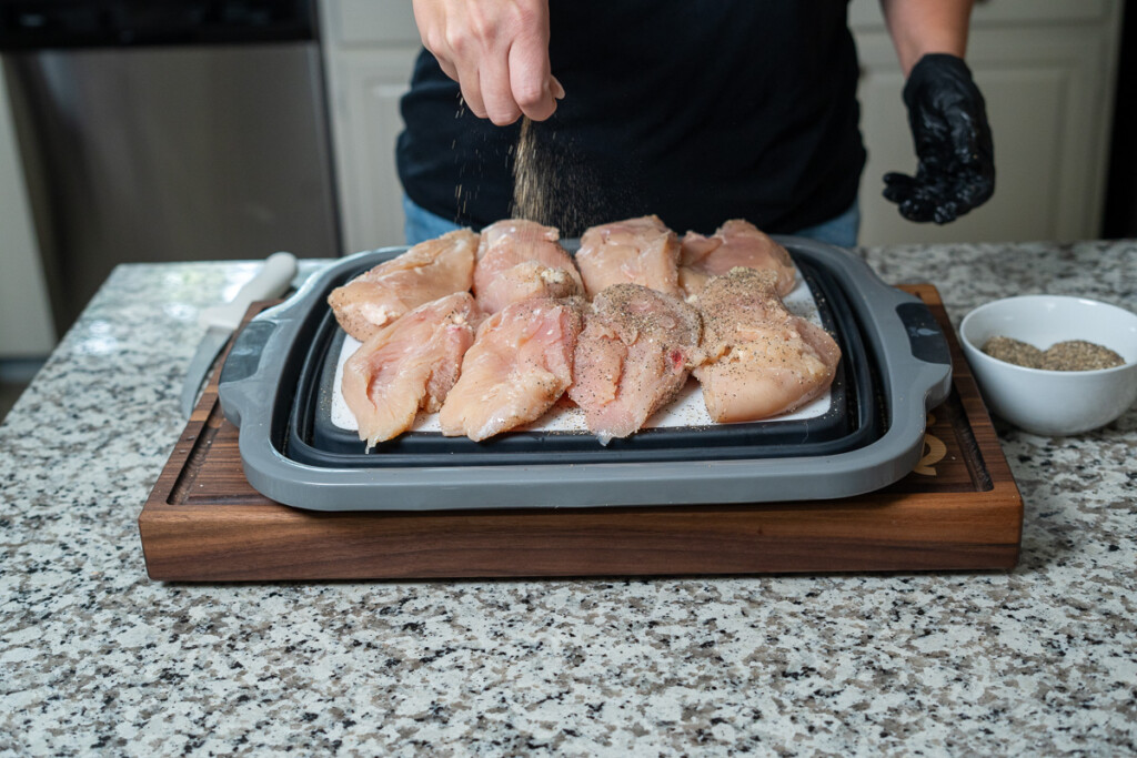 a hand sprinkling seasoning on raw chicken breasts