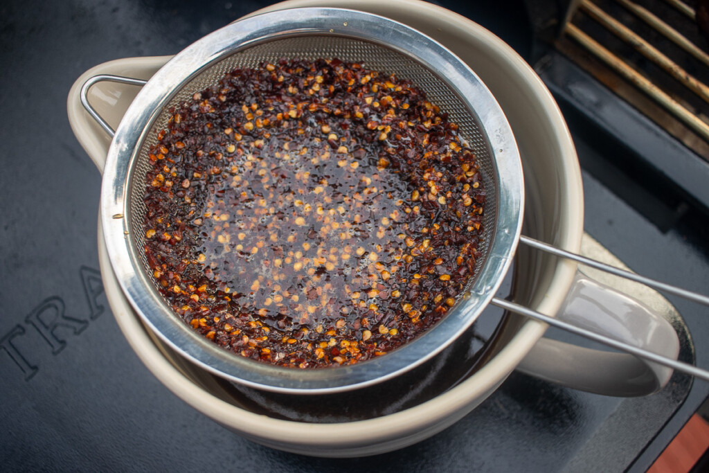 a sieve over a bowl, draining the hot honey