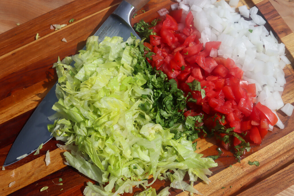 sliced lettuce and cilantro, diced tomato and onion on a wooden board