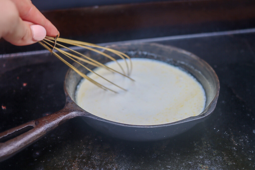 a skillet on the griddle with butter and cream being stirred with a whisk