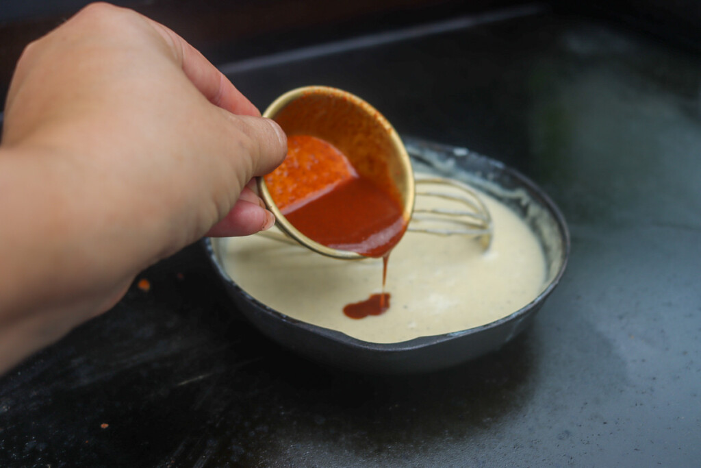 a skillet with queso in it and hot sauce being poured into it