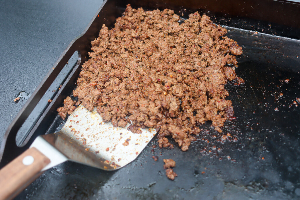 ground beef cooking on a griddle being stirred with a spatula