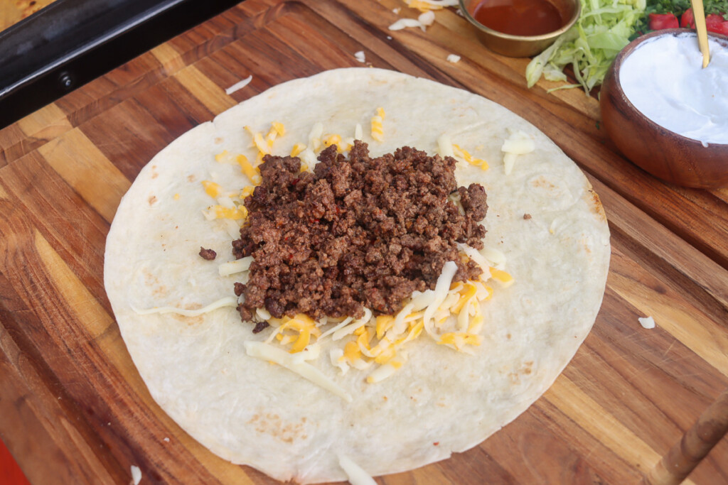 shredded cheese and cooked ground beef on a larg flour tortilla