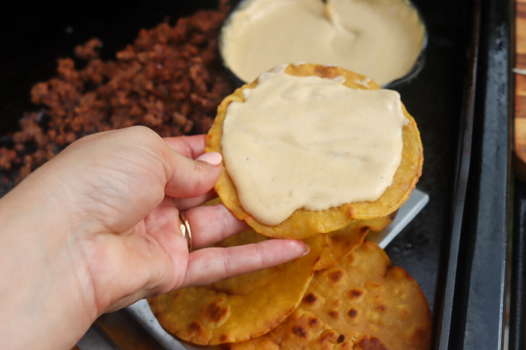 queso spread on a corn tortilla being held by a hand