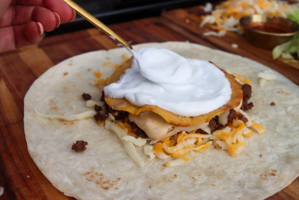 sour cream being spread over the corn tortilla which is sitting on the topping