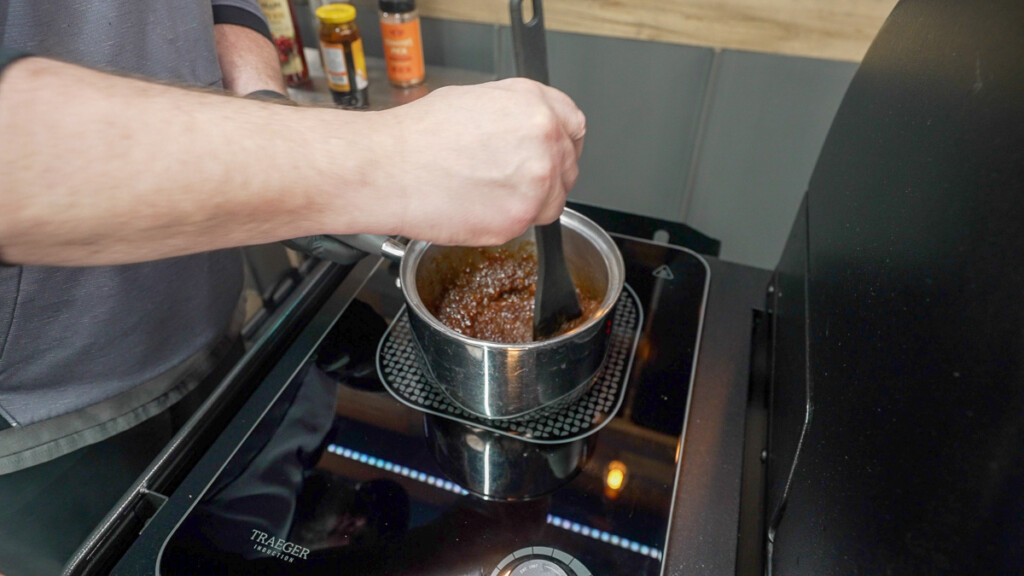 a hand holding a spoon stirring glaze in a pot