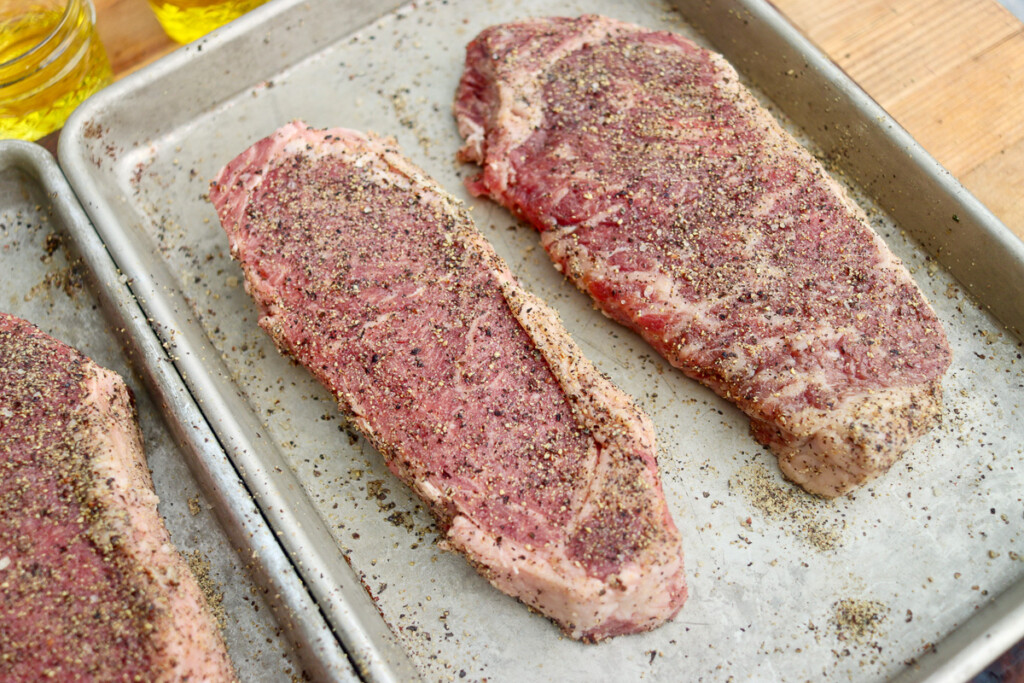 two raw seasoned steaks on a metal tray