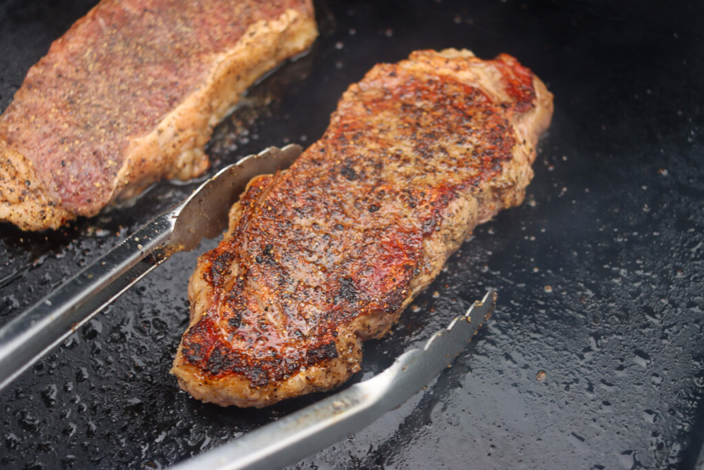 tongs turning a cooked steak on the griddle over