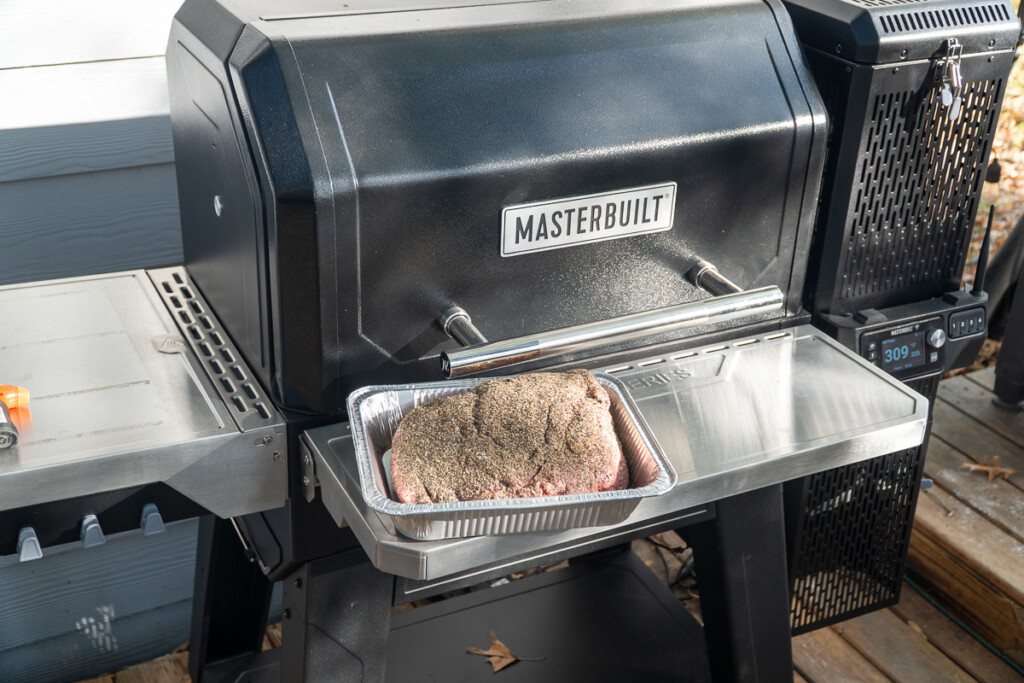 Seasoned meat in a foil tray on a Masterbuilt Gravity XT front shelf