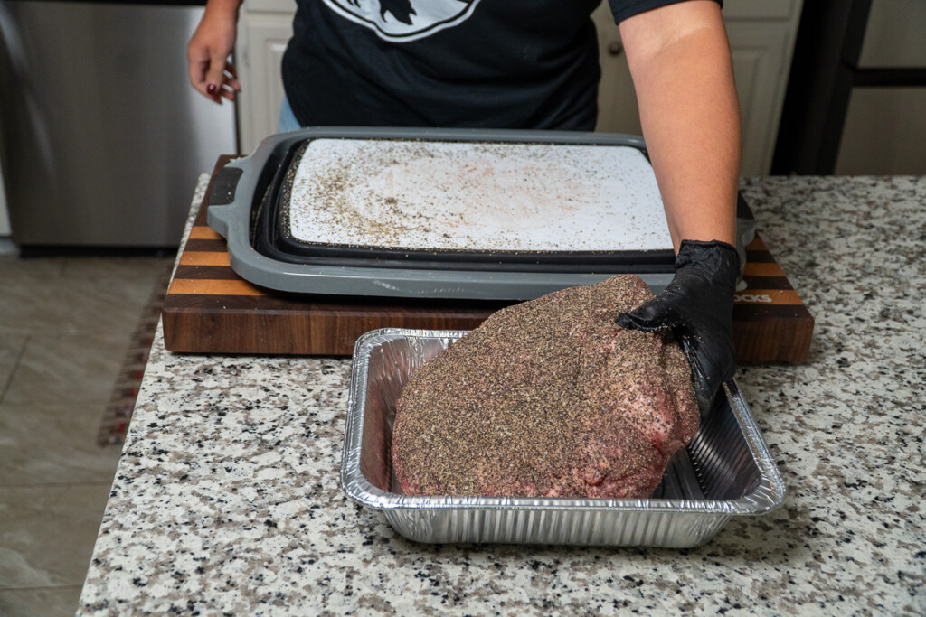 a person placing the seasoned raw pork butt into an aluminum tray