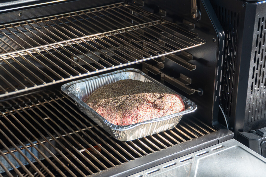 a raw seasoned pork butt in an aluminum tray in the smoker