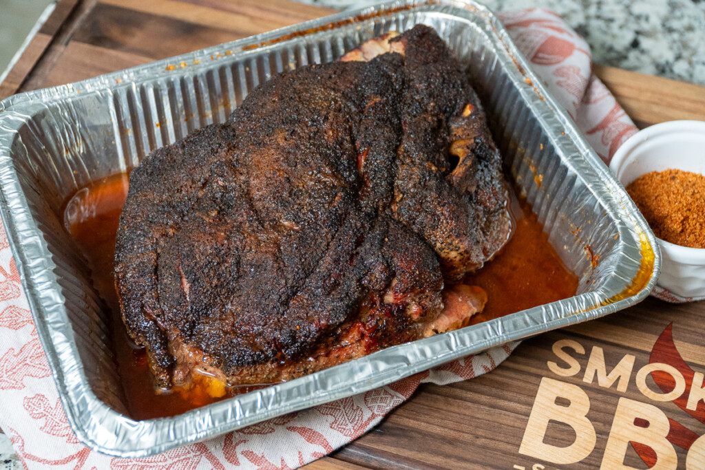 a cooked hot and fast pork butt resting on a smoked BBQ source cutting board