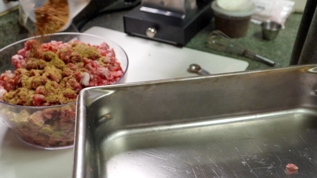 a metal tray in the foregroudna and a bowl of raw ground meat with seasoning on top