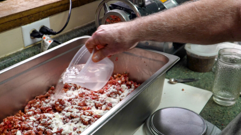 a hand holding a jug pour liquid over ground meat