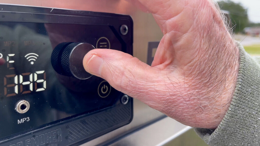 a hand setting the temperature on the smoker to 145°F 