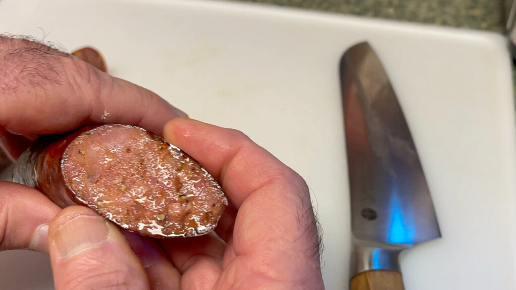 a hand holding a sliced texas hot gut sausage