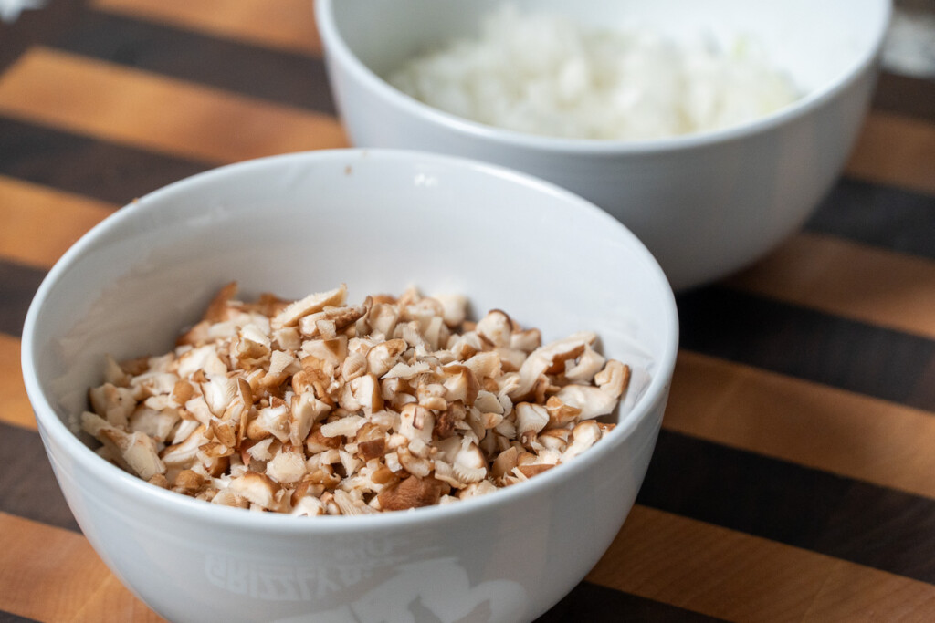 two white bowls, one with diced onion and the other diced mushrooms