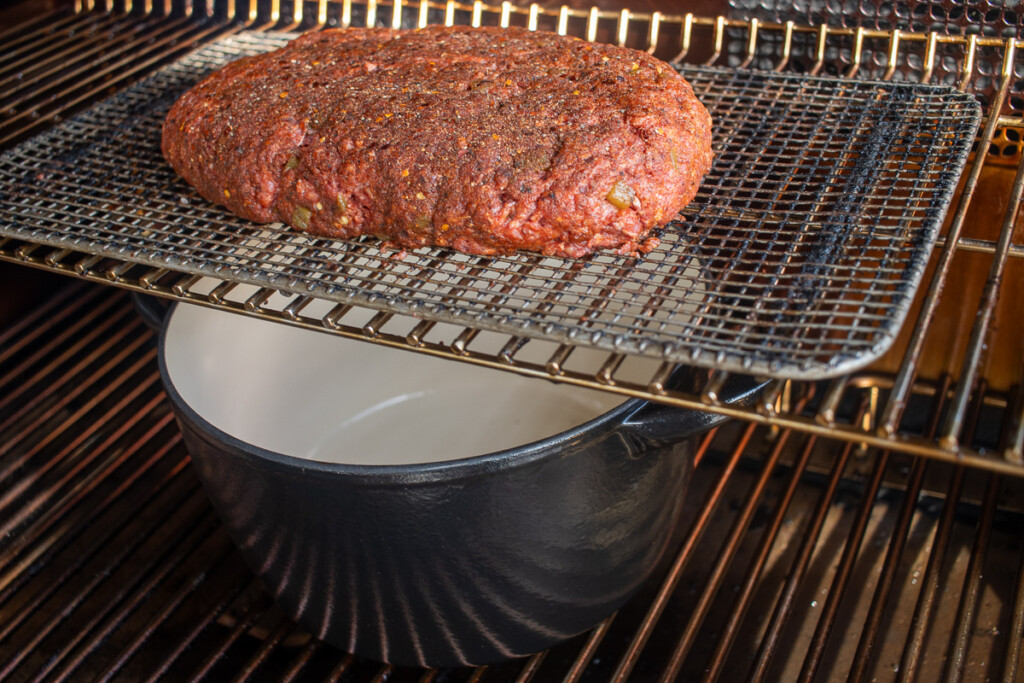 beef roll on a shelf in the smoker with a dutch oven underneath it