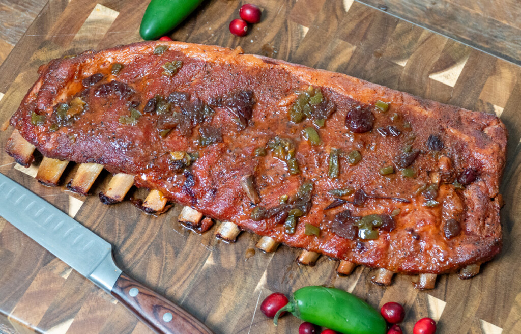 a rack of cranberry jalapeno glazed pork ribs on a wooden board with a knife