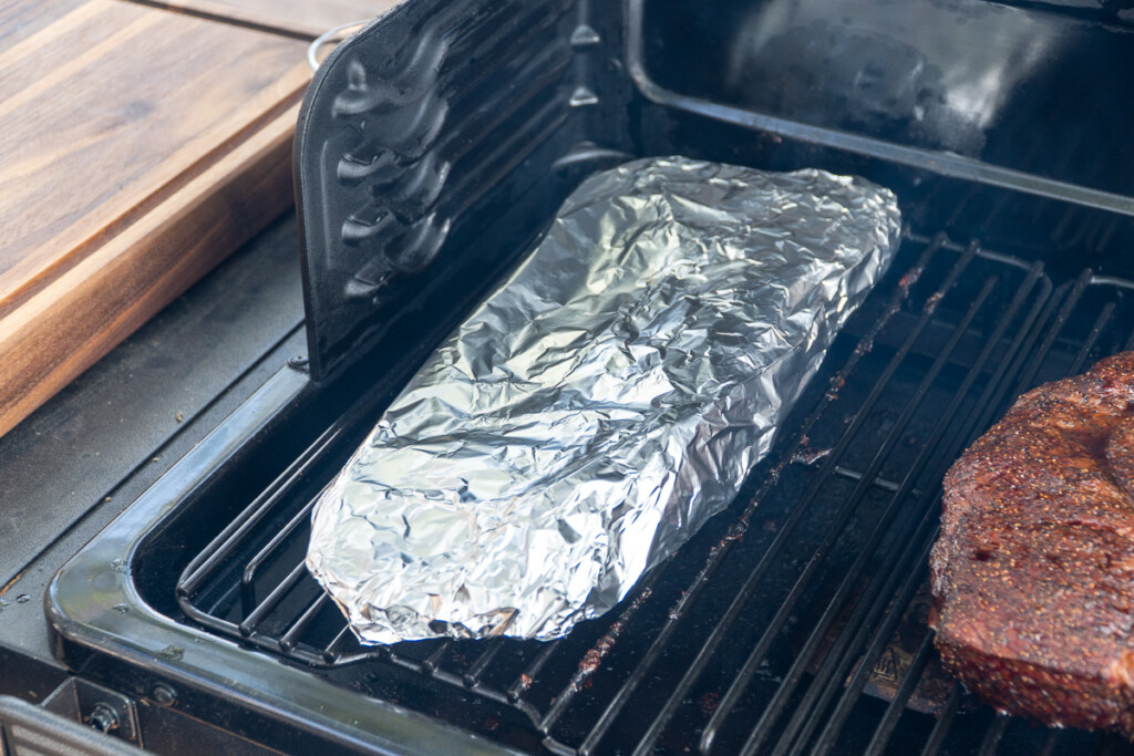 a rack of ribs wrapped in foil in the smoker